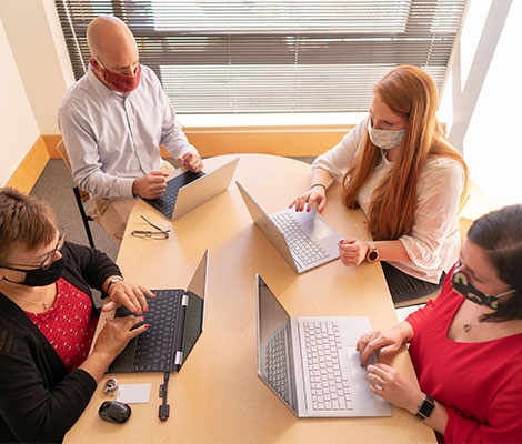 Four coworkers around a conference table while typing on their laptops.