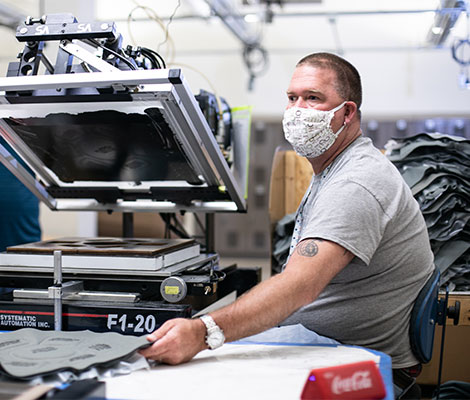 A man in a grey shirt and face mask operates a printing machine.