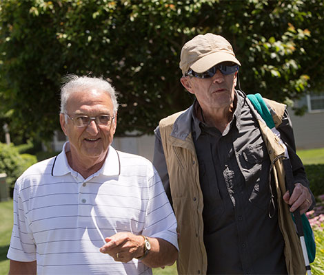 An older man volunteers to help provide sighted guide to a middle aged male client.