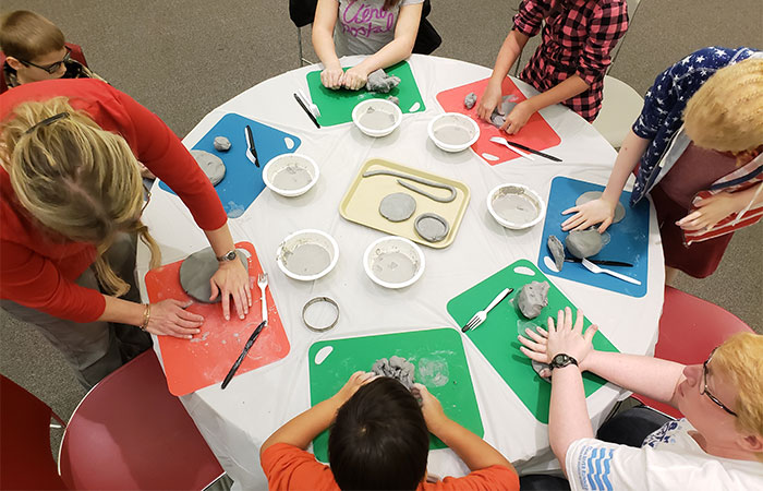 A table with children around it working with clay is photographed from overhead.